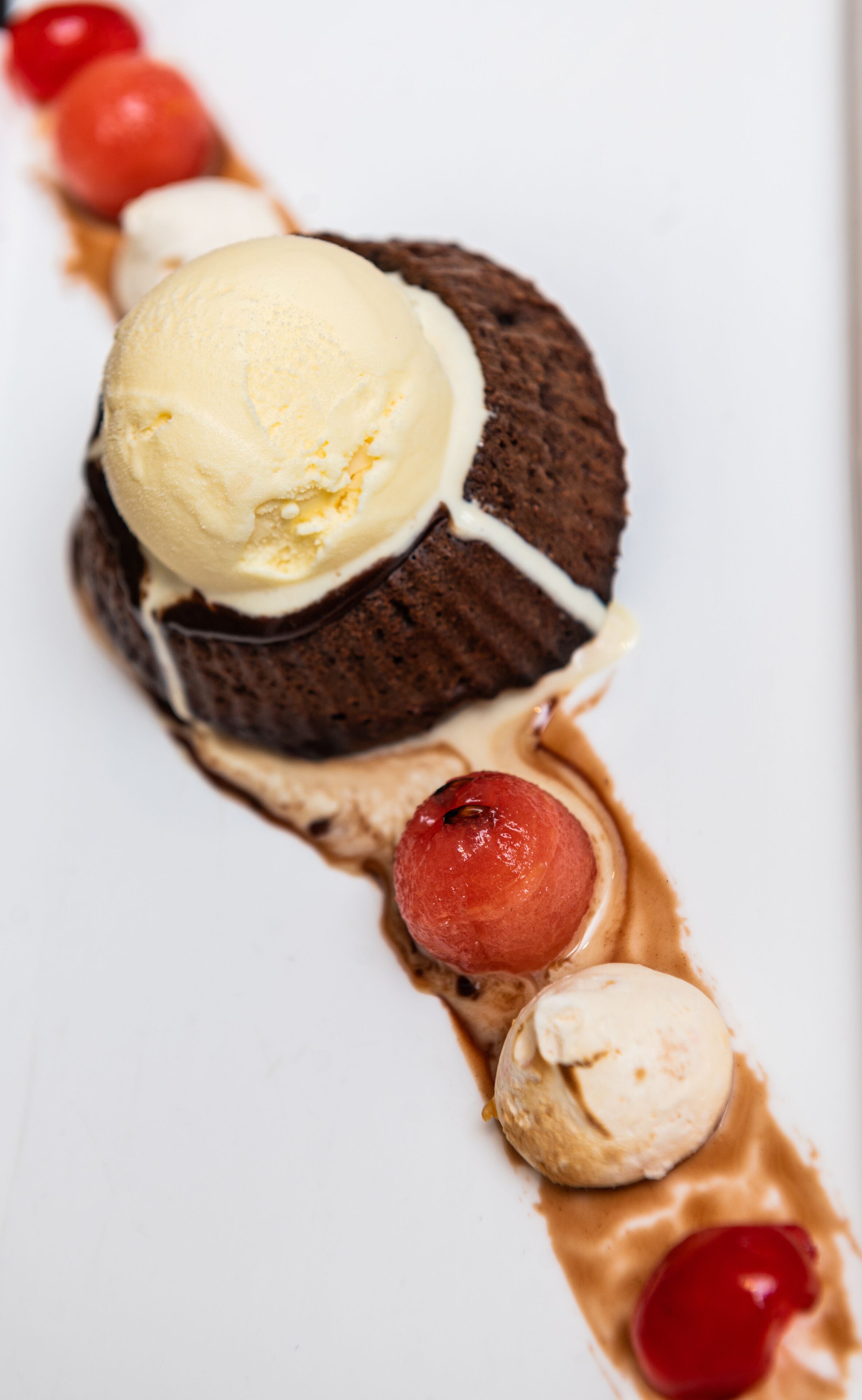 Un postre con helado, pastel de chocolate y cerezas sobre un plato blanco.