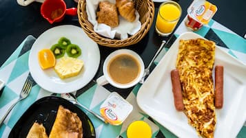 Une table de petit-déjeuner avec des croissants, des fruits, des saucisses, une omelette, du café, du jus de fruits et du yaourt.