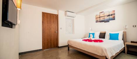 A hotel room with a bed, a TV mounted on the wall, an air conditioning unit, and a painting above the bed.