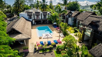 Un resort con piscina rodeada de sillones de descanso y construcciones de techo de paja.