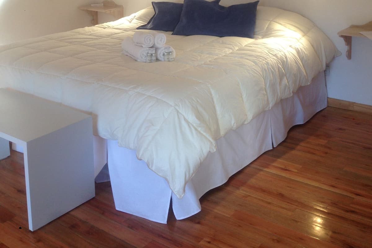 A bedroom with a large bed, white bedding, and a small bedside table.