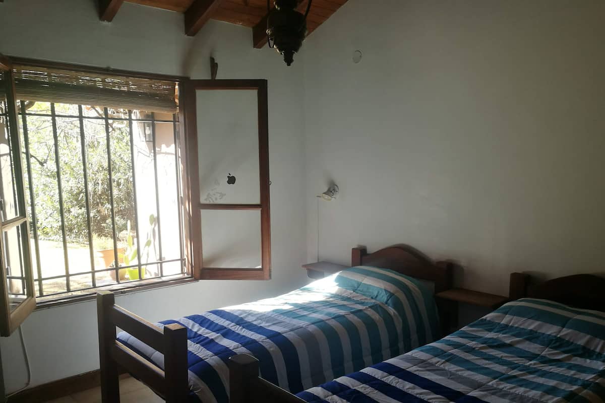 A room with two beds, a window with bars, a wooden ceiling, and a hanging light fixture.