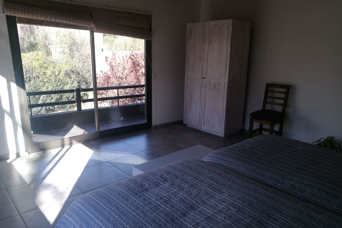 A bedroom with a bed, a wardrobe, a chair, and a balcony with a view of trees.