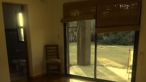 Camera da letto con un letto grande, una sedia e vista su una zona esterna tramite una porta finestra.