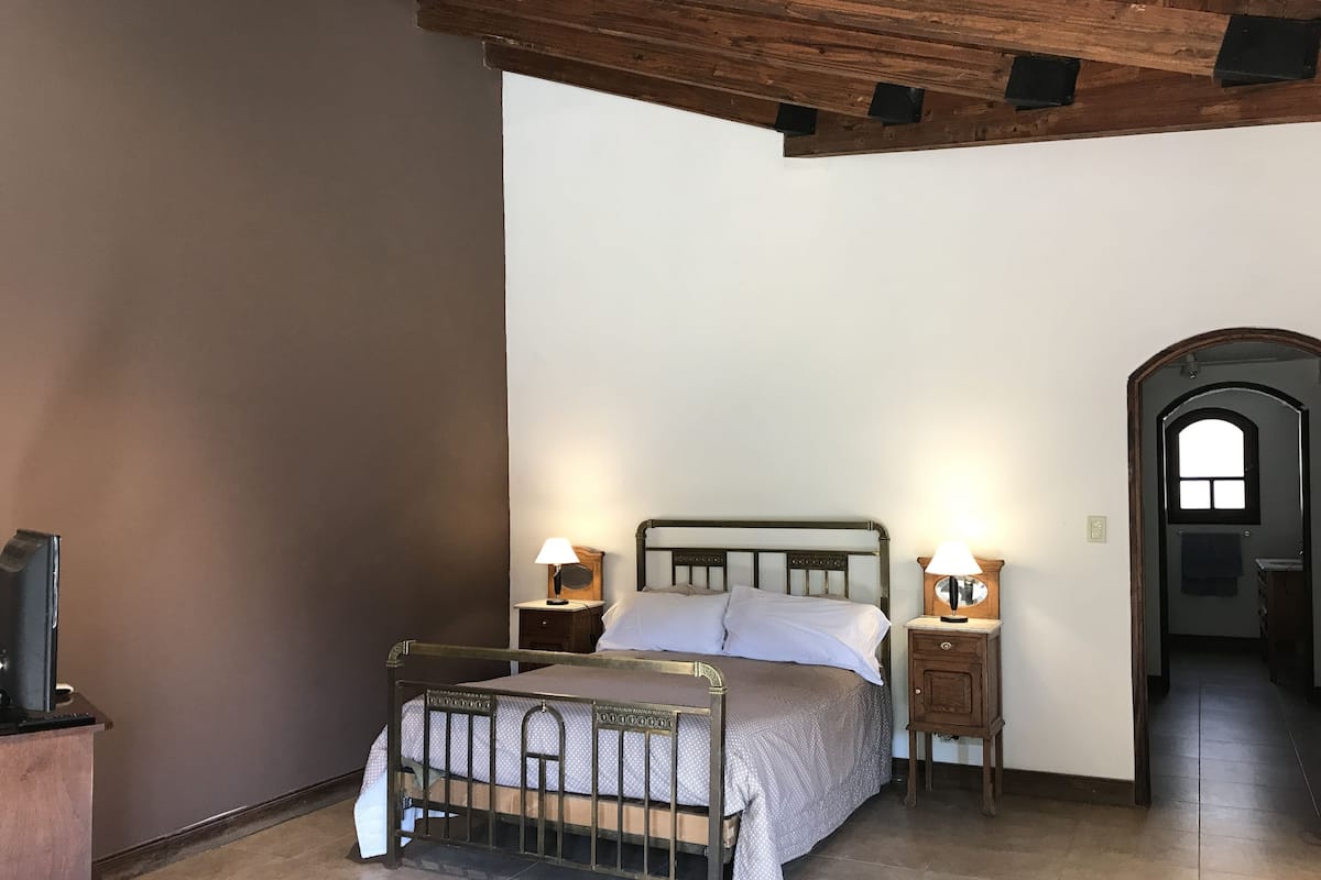 A bedroom with a bed, two bedside tables with lamps, a wooden headboard, and a dark wooden door with a window.