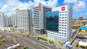 A modern hotel complex with multiple high-rise buildings, a parking area, and a road with vehicles. - NB Hotéis (Aracaju)