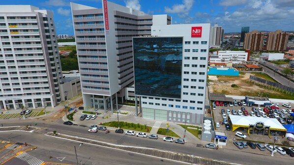 A modern hotel with multiple floors, a prominent glass facade, and a parking lot with several cars. - NB Hotéis (Aracaju)