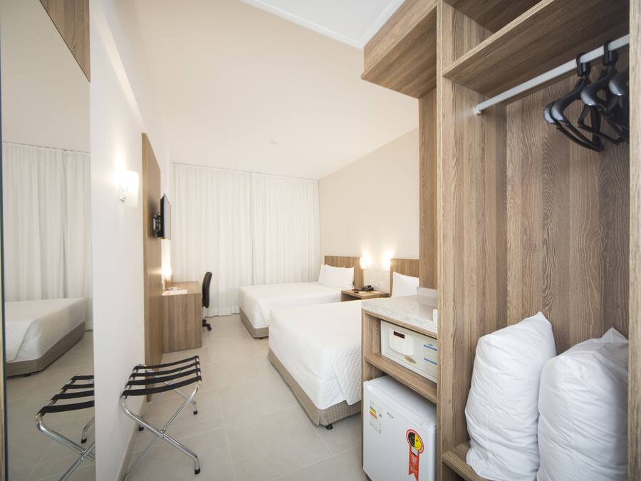 A hotel room with two beds, a desk, a chair, a wardrobe, and a small refrigerator.