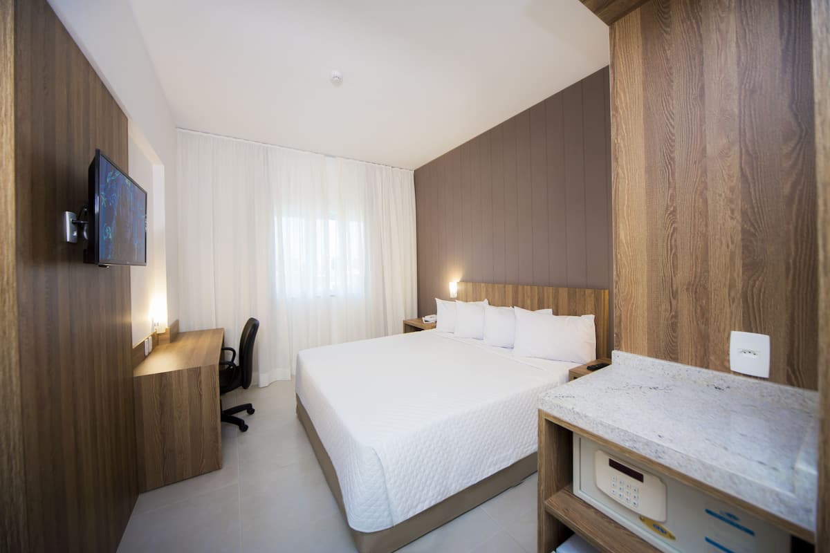 A modern hotel room with a large bed, a desk, a television, and a marble countertop.