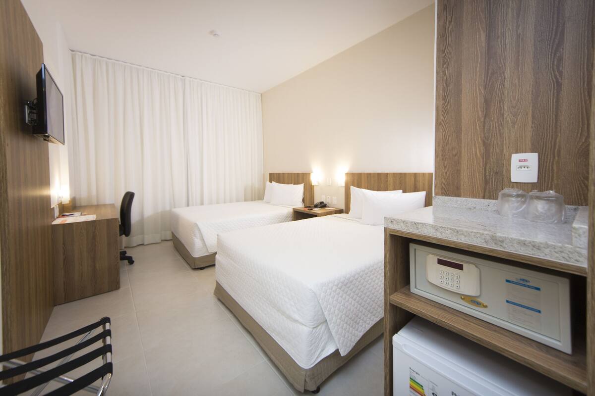 A hotel room with two beds, a desk, a chair, a TV, and a minibar.
