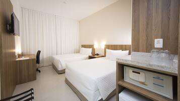 A hotel room with two beds, a desk, a chair, a TV, and a minibar.