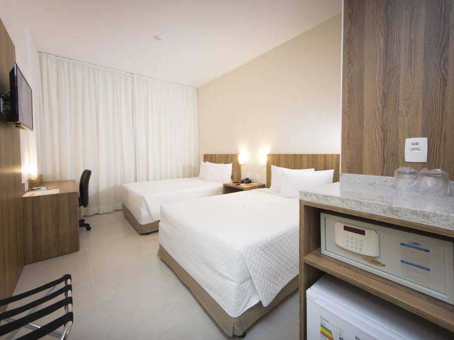 A hotel room with two beds, a desk, a chair, a TV, and a minibar.