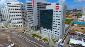 A modern building with multiple floors, a prominent 'NB' logo on the side, and a parking lot in front. - NB Hotéis (Aracaju)