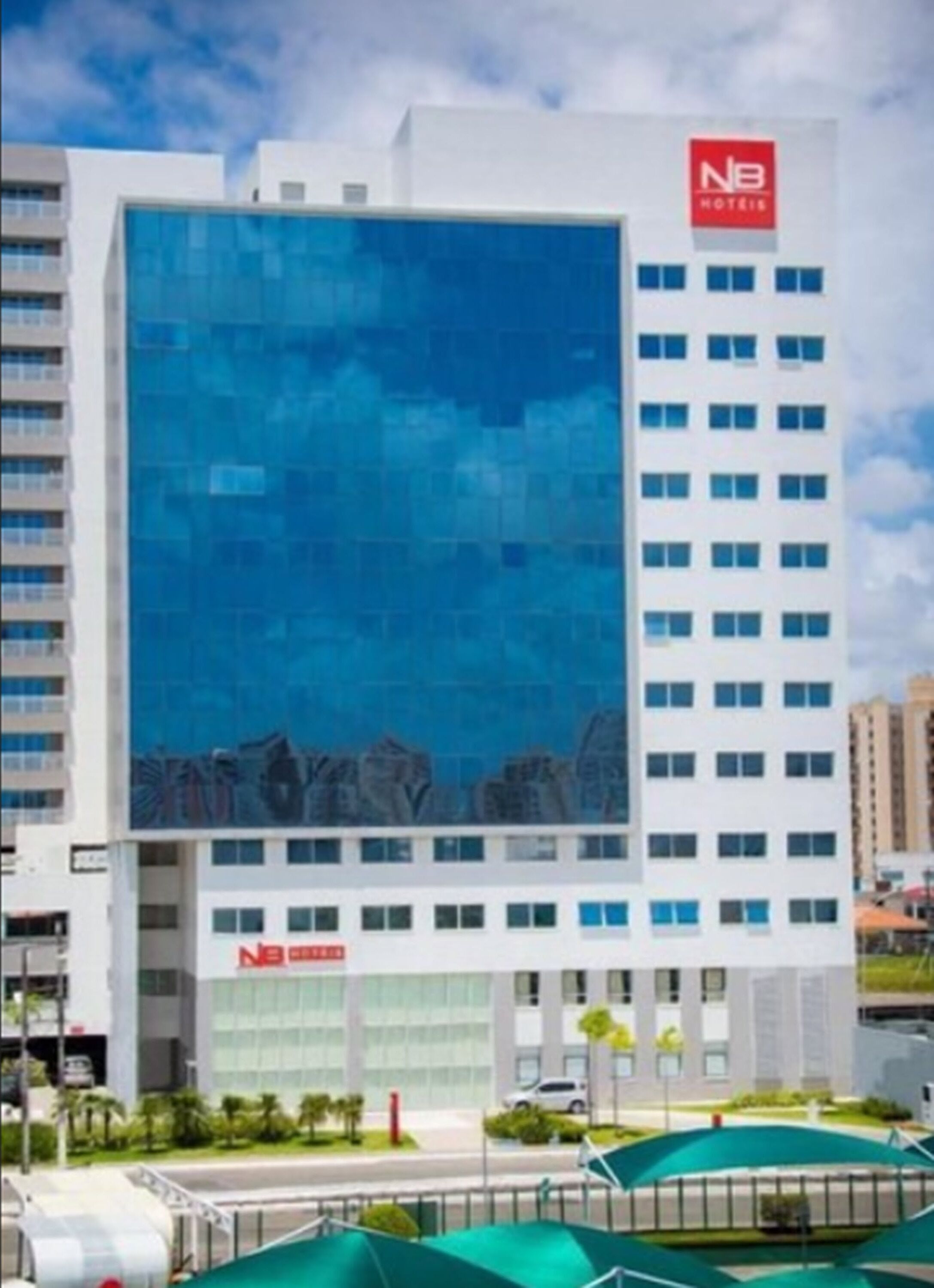 Un moderno edificio de hotel con una destacada fachada de vidrio, varios pisos y un área de piscina en la azotea.