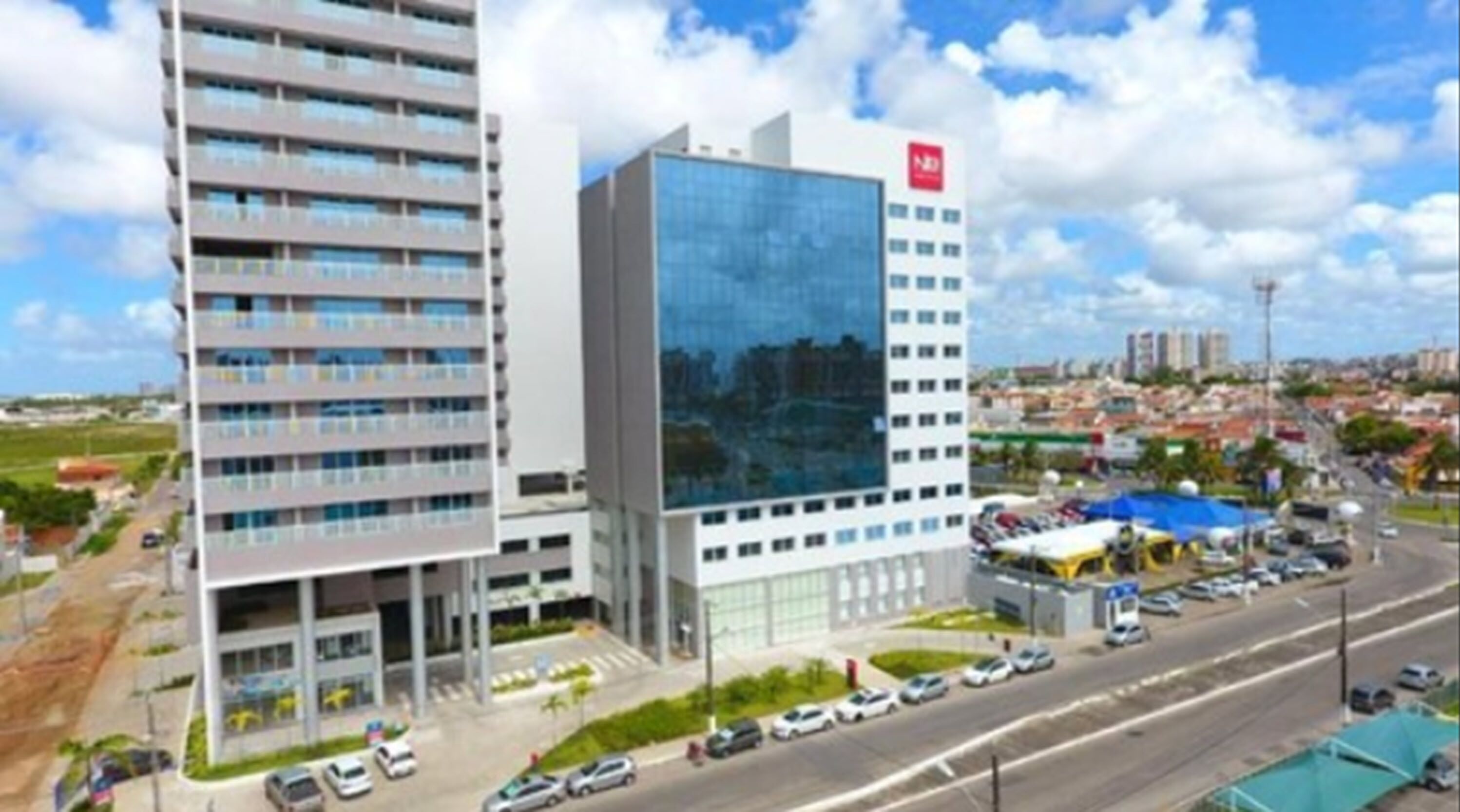 A modern hotel with a glass facade, multiple floors, and a parking lot with cars.