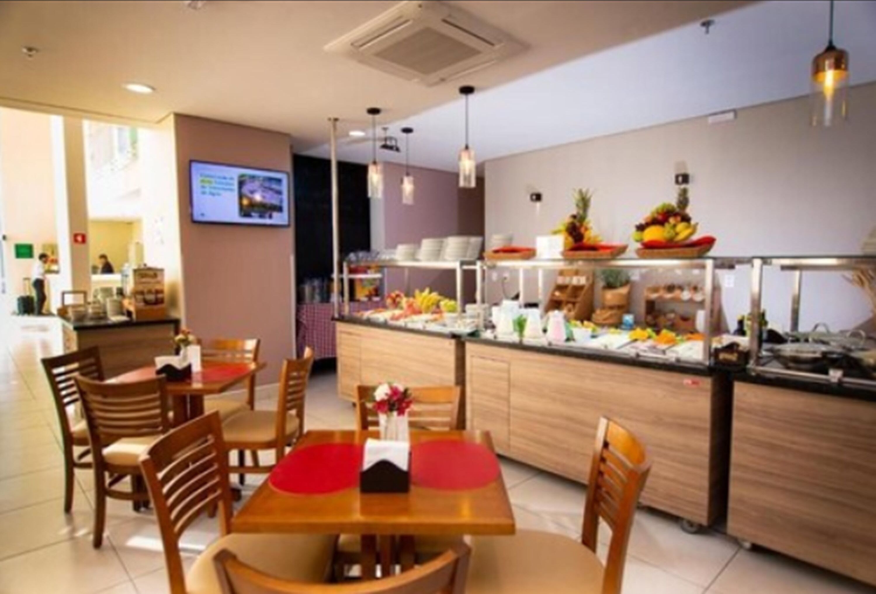 Uma sala de jantar de hotel com mesas e cadeiras de madeira, um balcão de buffet com diversos alimentos e um design de interiores moderno.