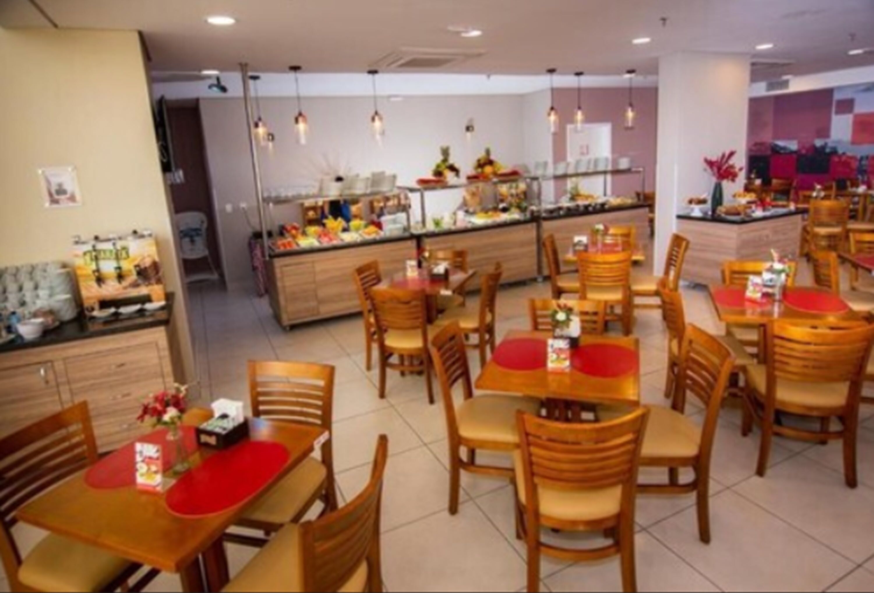 A dining area with wooden tables and chairs, a buffet counter with various food items, and hanging pendant lights.