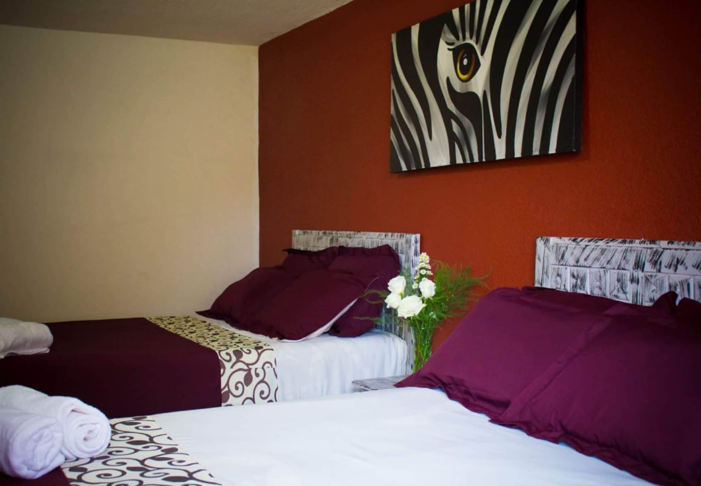 Habitación de hotel con dos camas, cada una con una colcha estampada, cabecero con diseño texturizado y una obra de arte con estampado de cebra colgada en la pared.