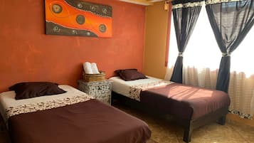 A room with two beds, a painting on the wall, and curtains on the window.