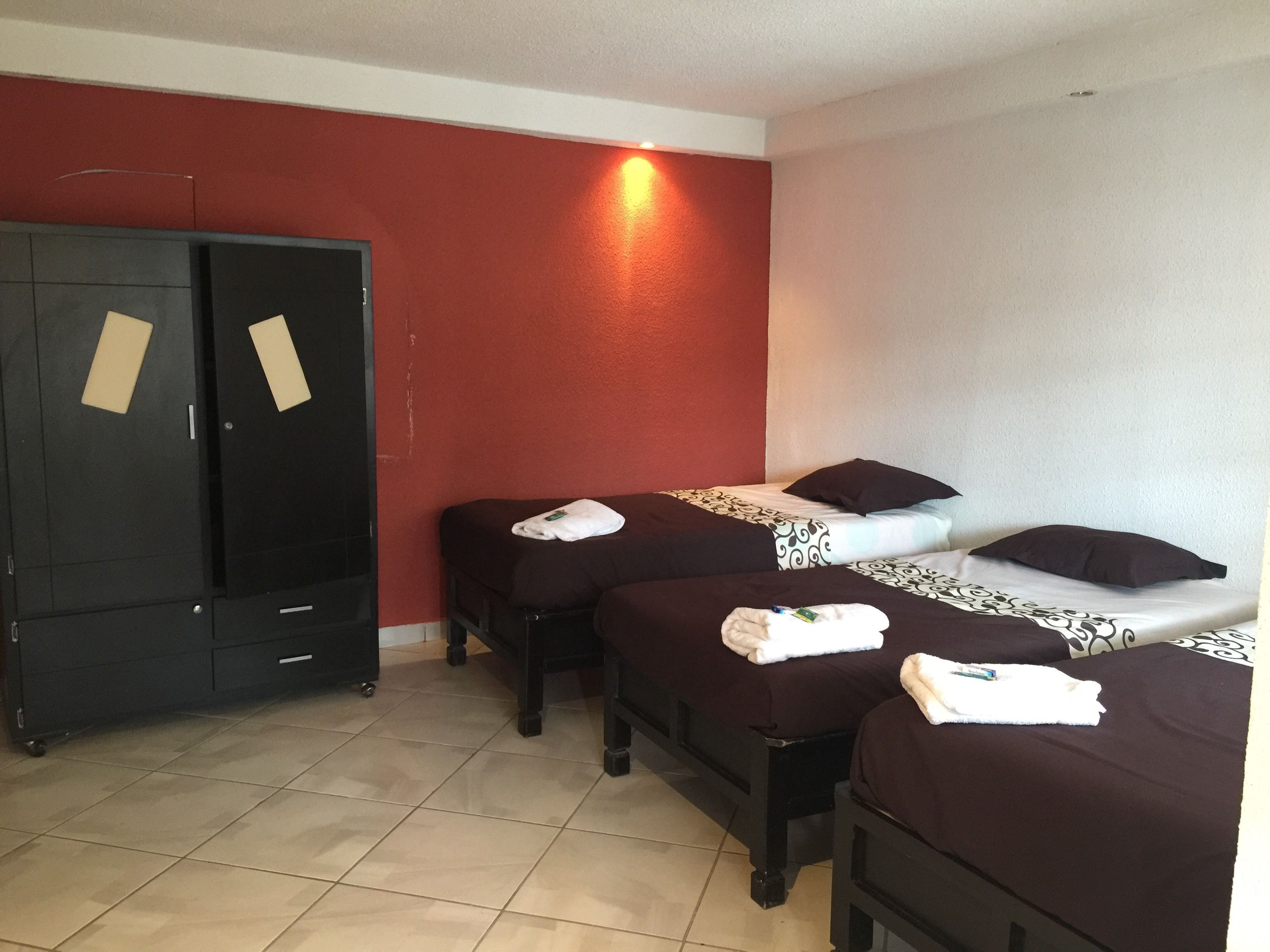 Quarto de hotel com duas camas de solteiro, um guarda-roupa e uma parede com detalhe em vermelho.
