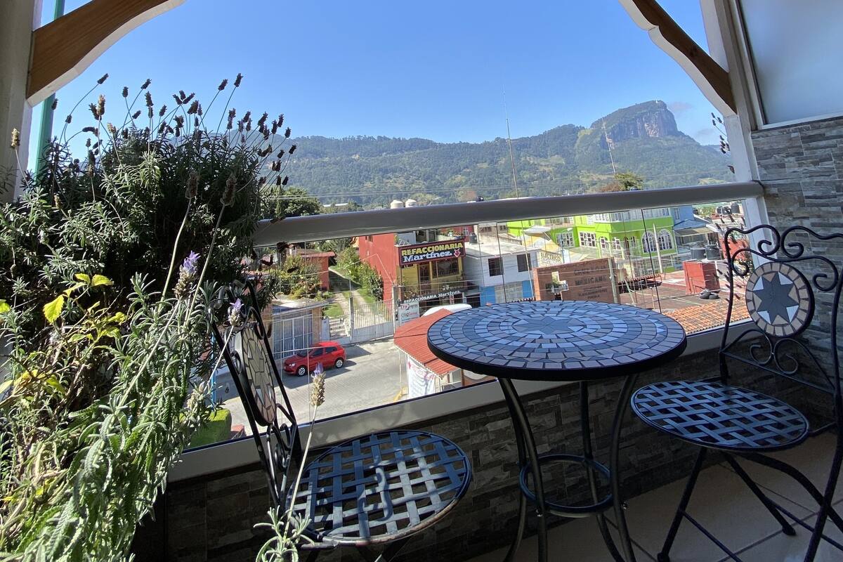 Une terrasse extérieure dotée d’un plafond en bois, d’une table ronde, de deux chaises et offrant une vue sur une chaîne de montagnes.