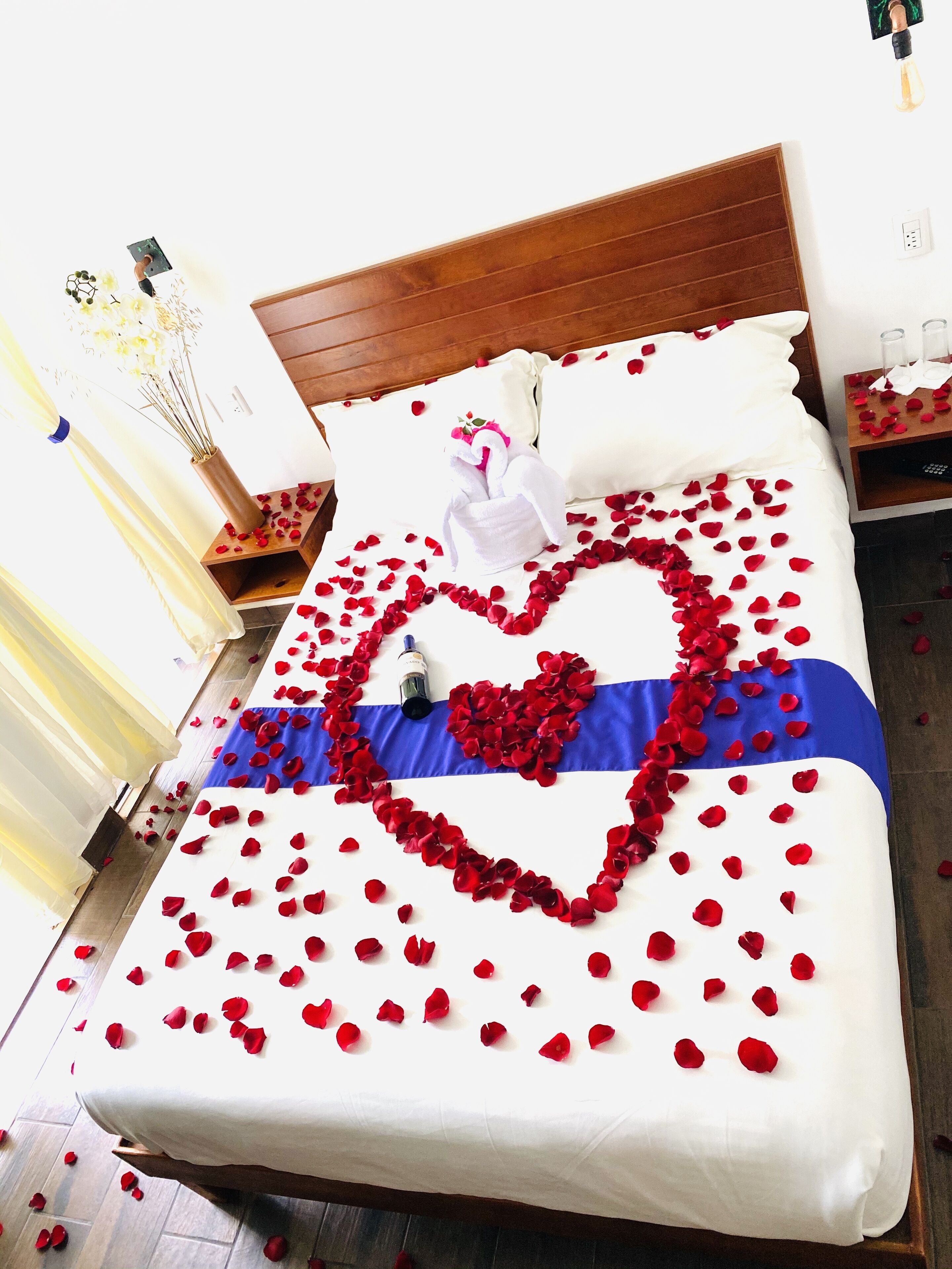 Een bed met een hartvormige bloemstuk van rozenblaadjes en een blauw-witte strepen deken.