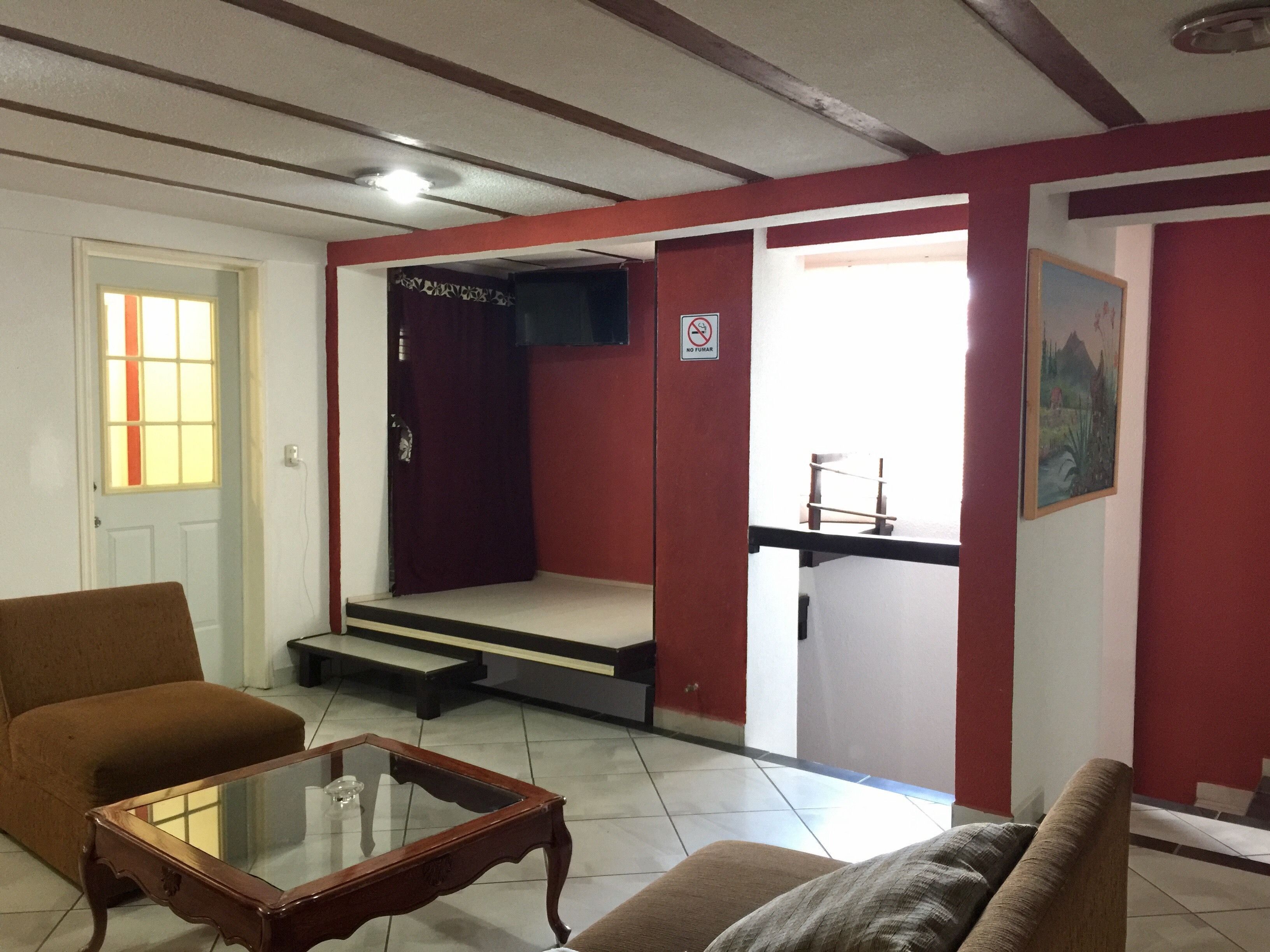 A living room with a brown sofa, a glass-top coffee table, and a red wall. There is a door leading to another room and a painting on the wall.