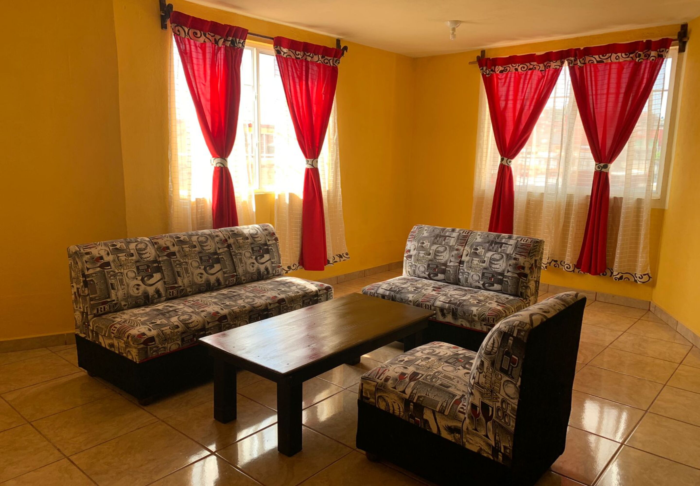 A room with two patterned sofas, a wooden coffee table, and red curtains.