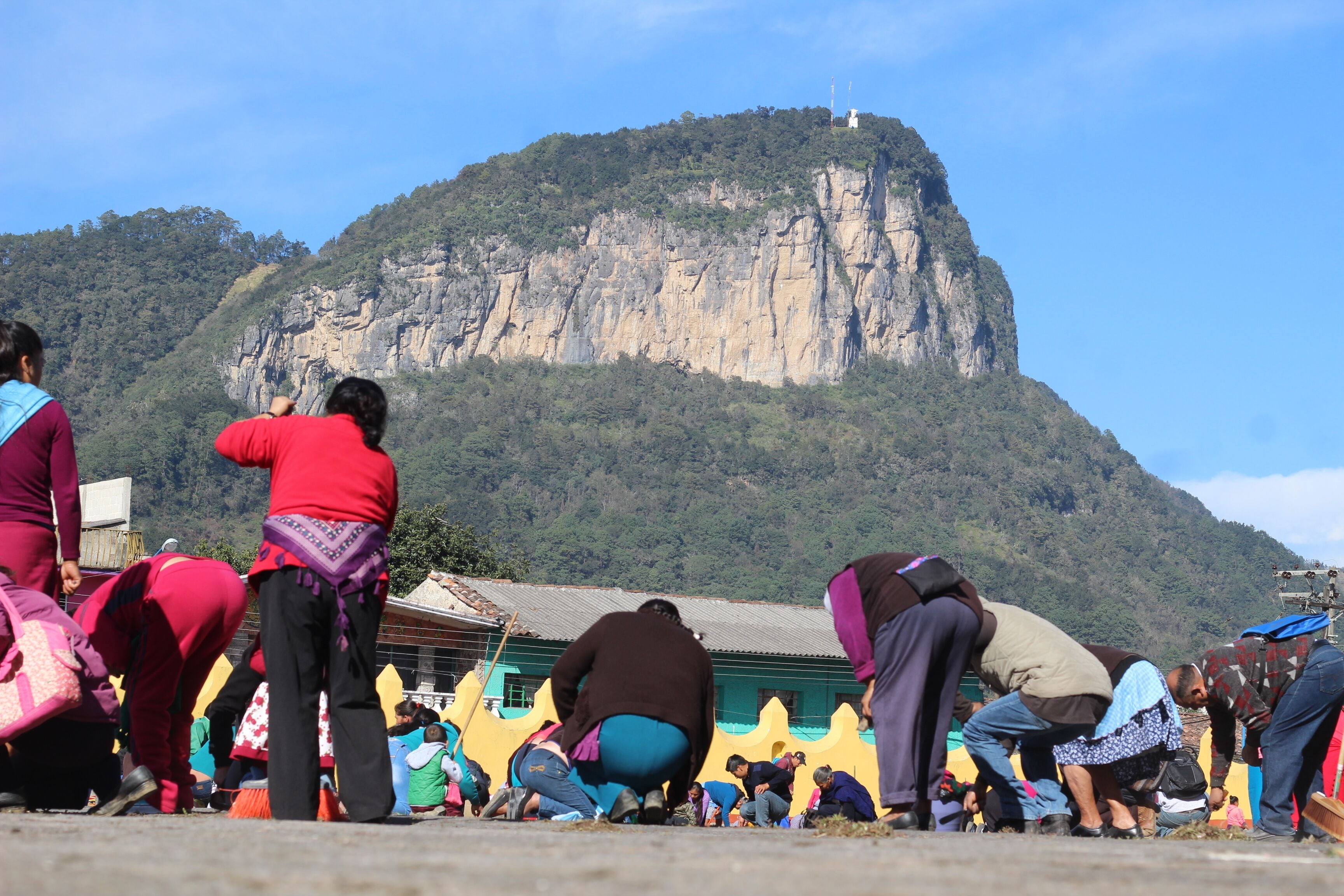 A group of people gathered around a building with a mountain in the background.