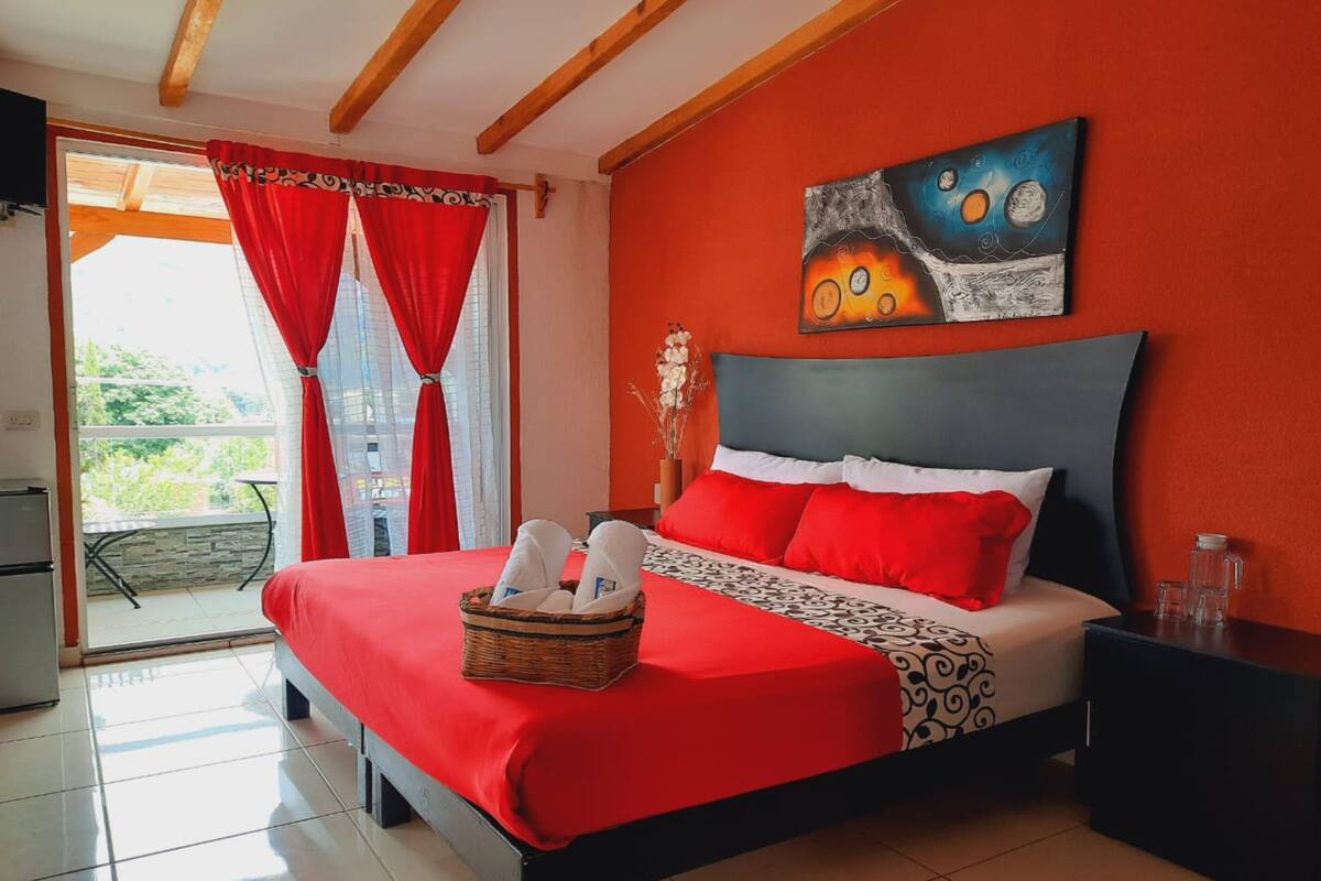 Une chambre d’hôtel avec un grand lit, des rideaux rouges, un tableau au mur et un balcon avec vue.