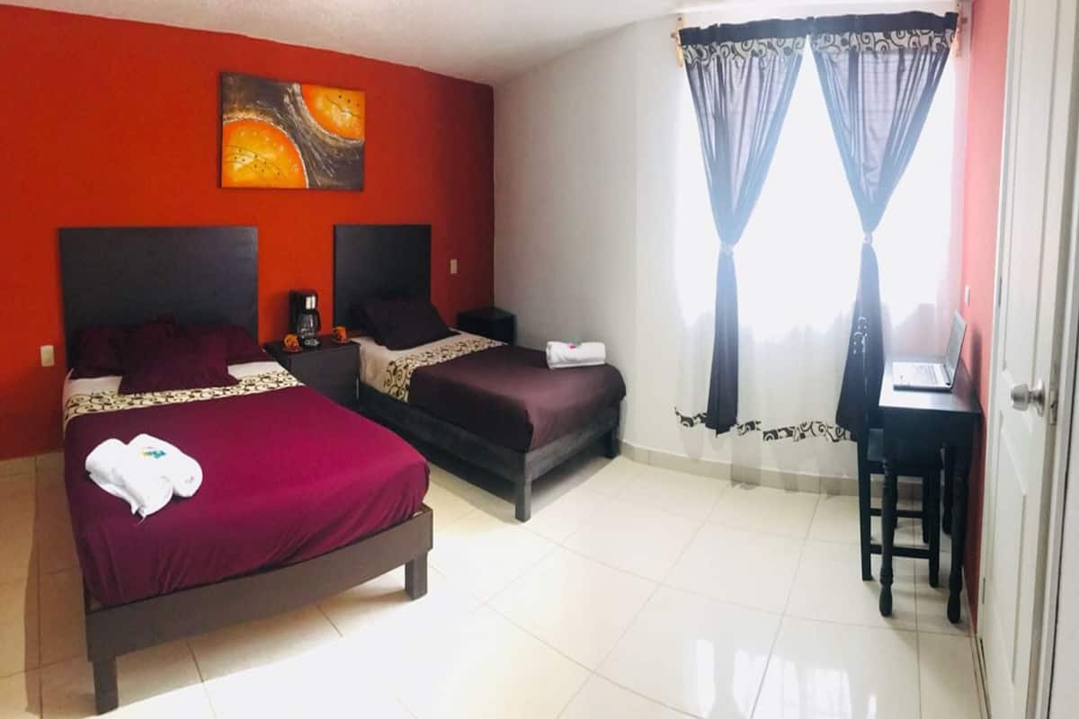 Une chambre d’hôtel avec deux lits, un bureau et une fenêtre avec des rideaux.