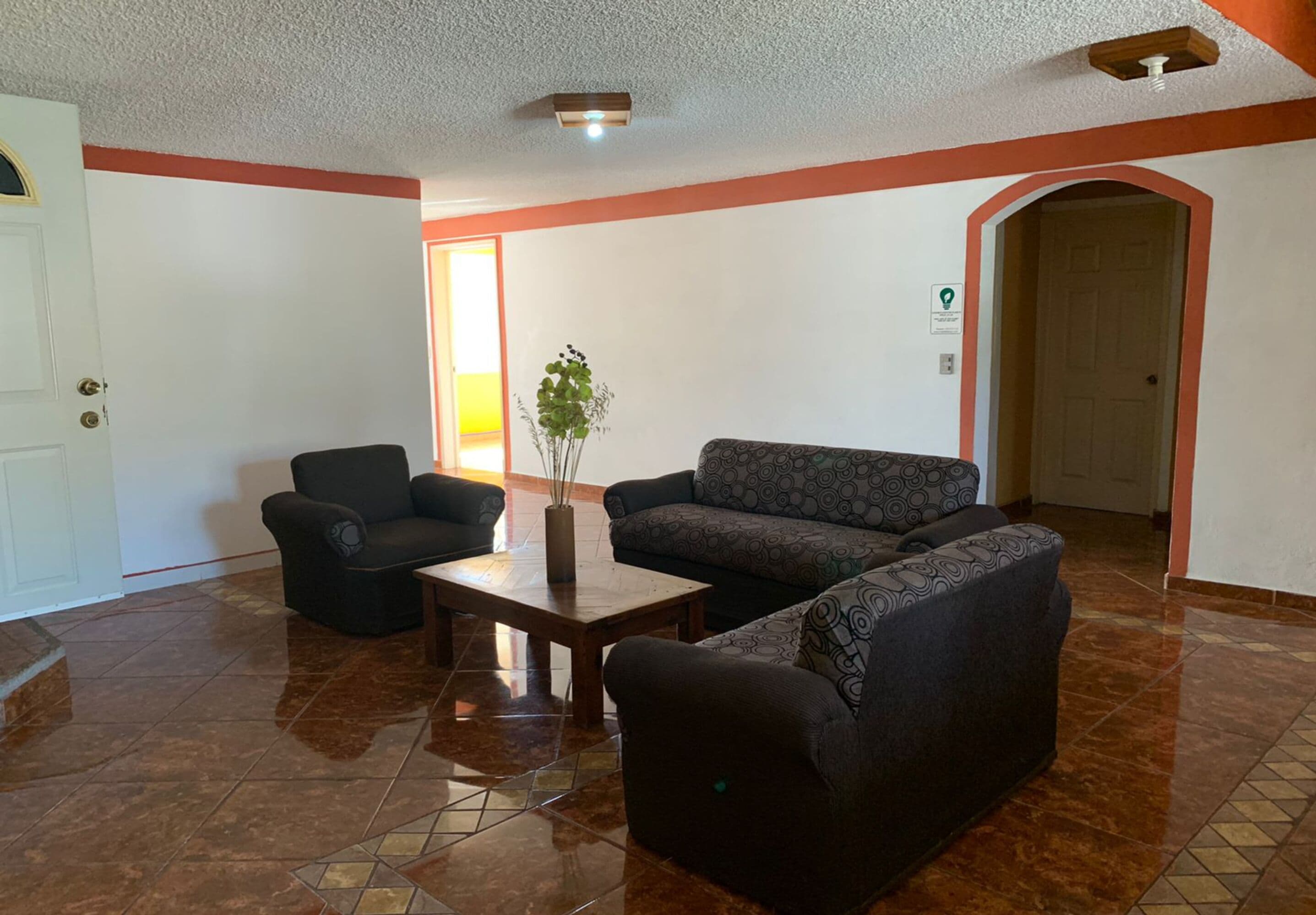 A lobby with a tiled floor, a sofa, a chair, and a small table with a vase.