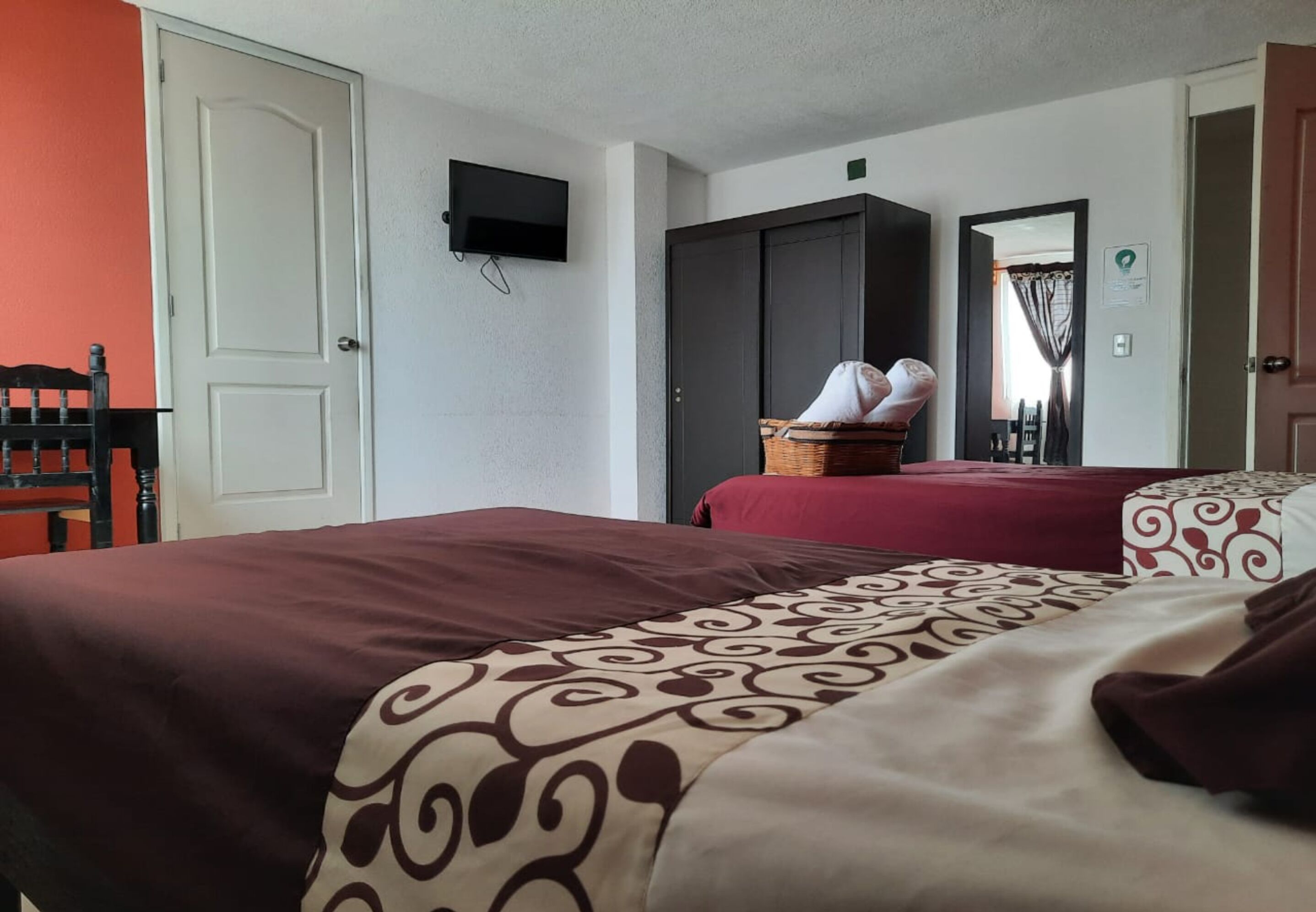 A hotel room with two beds, a wardrobe, a television, and a mirror.