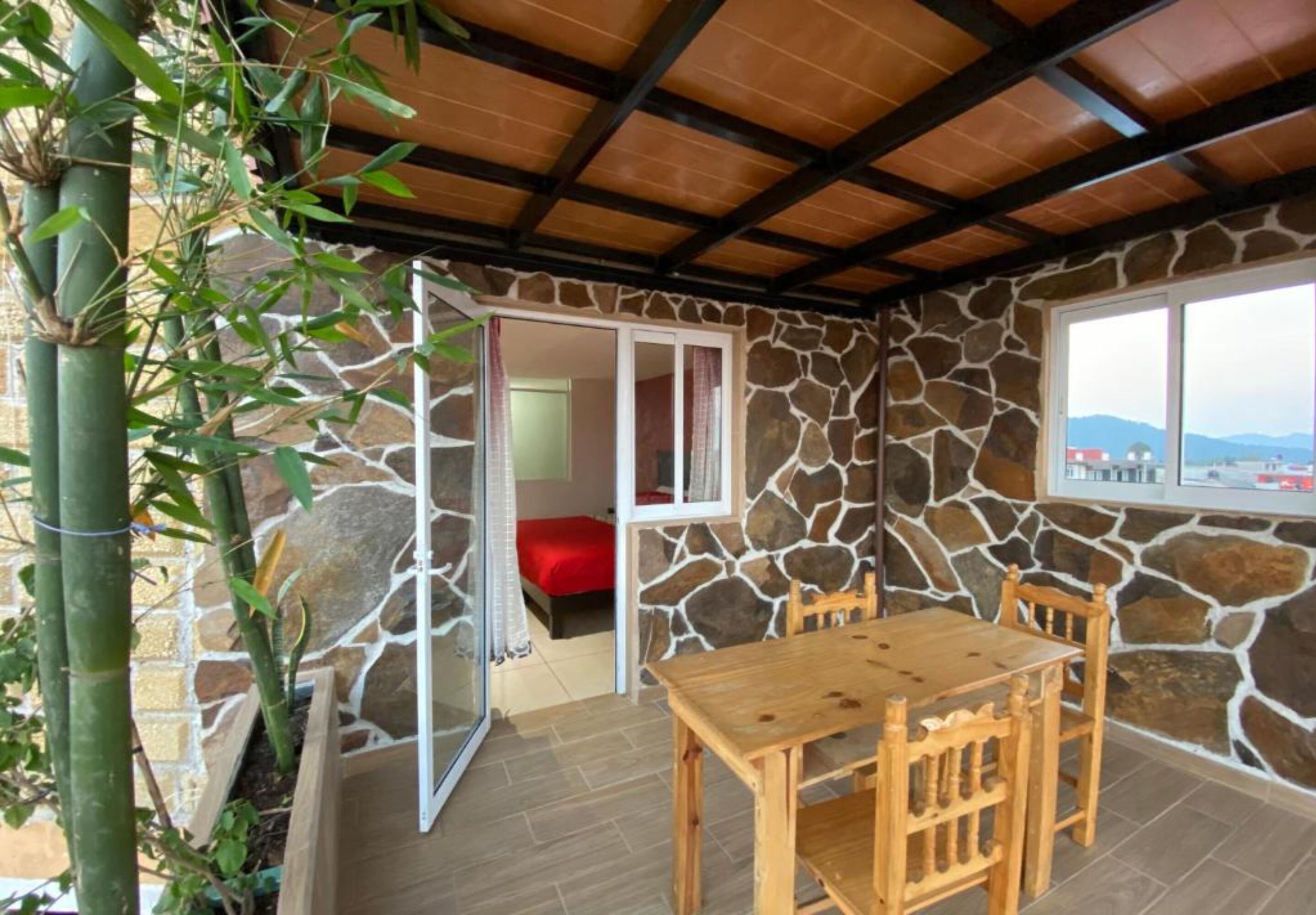 A room with a stone wall, a wooden table, and a red bed.