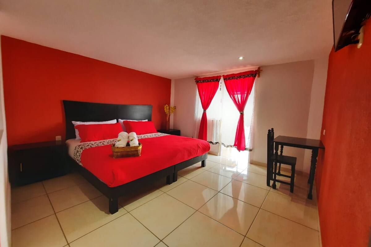 Une chambre avec un lit rouge et noir, une petite table et une chaise.