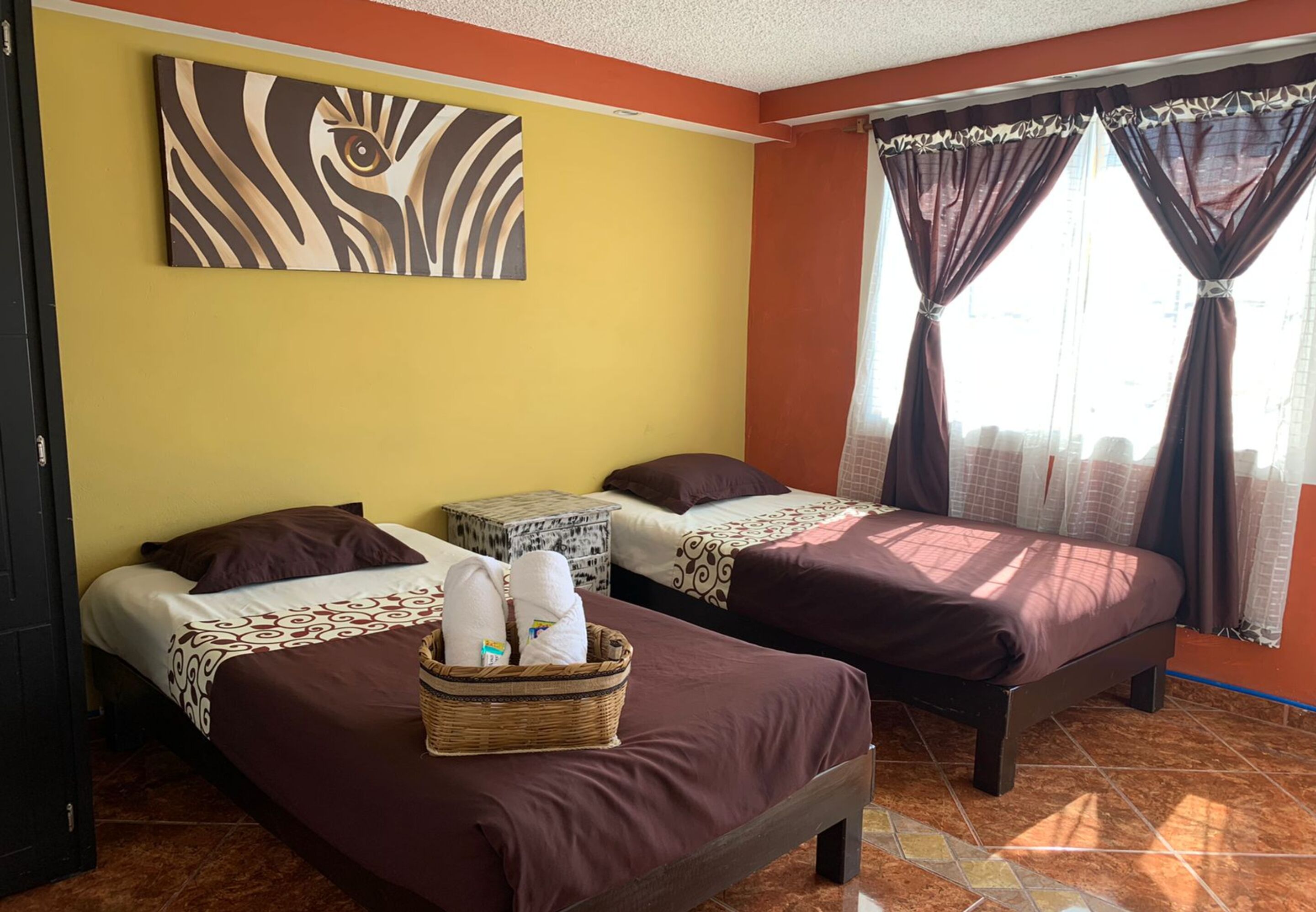 Una habitación de hotel con dos camas, una obra de arte en la pared y una ventana con cortinas.