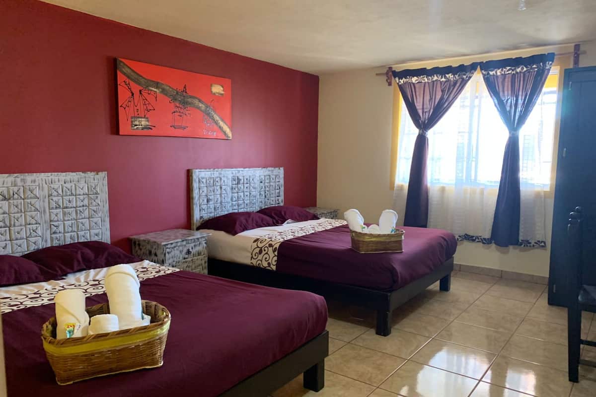 Une chambre d’hôtel avec deux lits, chacun doté d’une tête de lit, un mur rouge, un tableau et une fenêtre avec des rideaux.