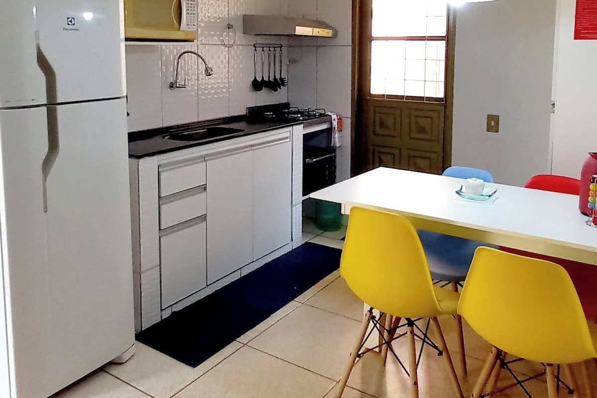 Une cuisine compacte avec des meubles blancs, un réfrigérateur blanc, une table jaune assortie de chaises, et une fenêtre donnant sur un beau paysage.