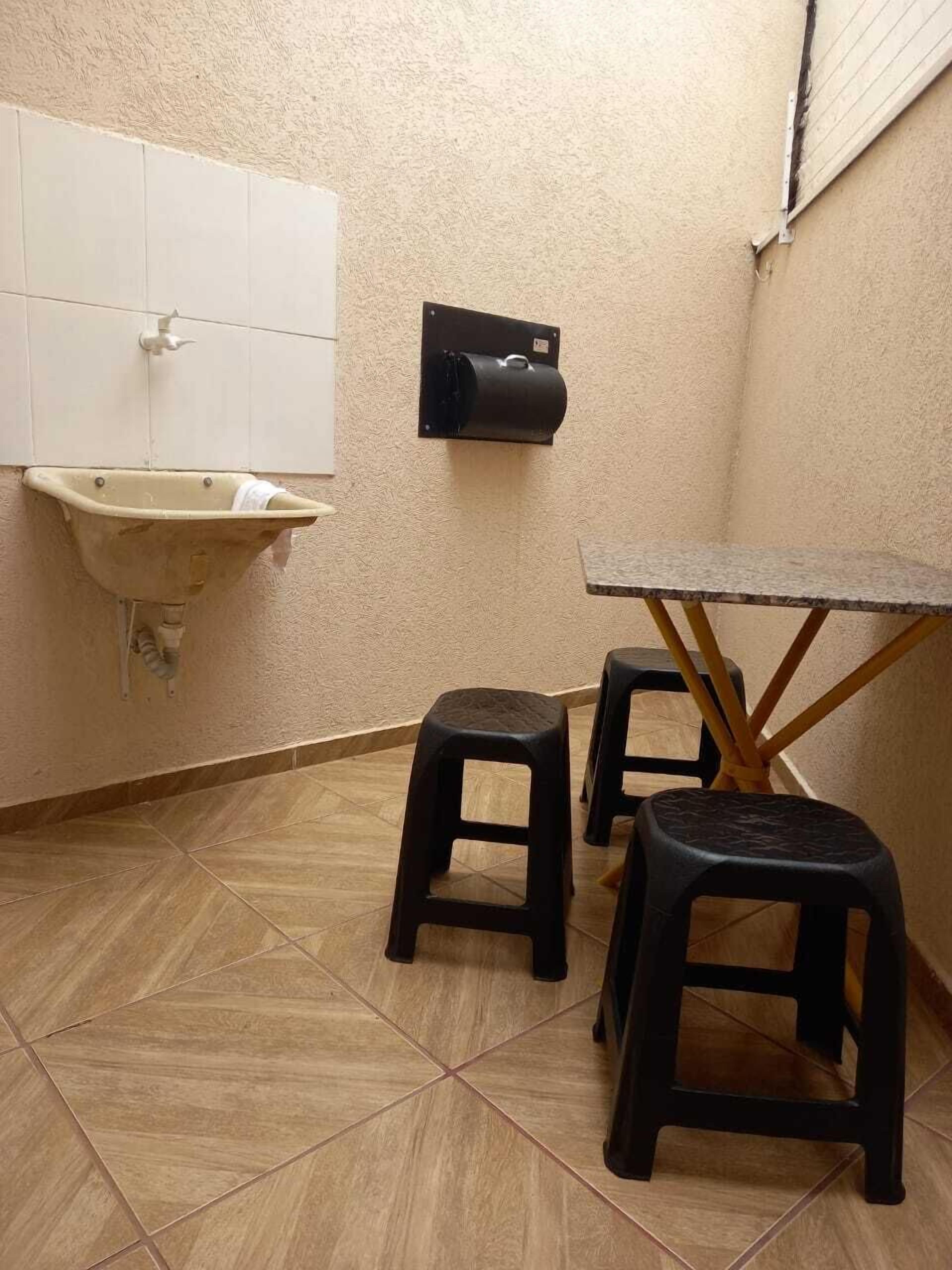 A small room with a sink, two stools, and a table.