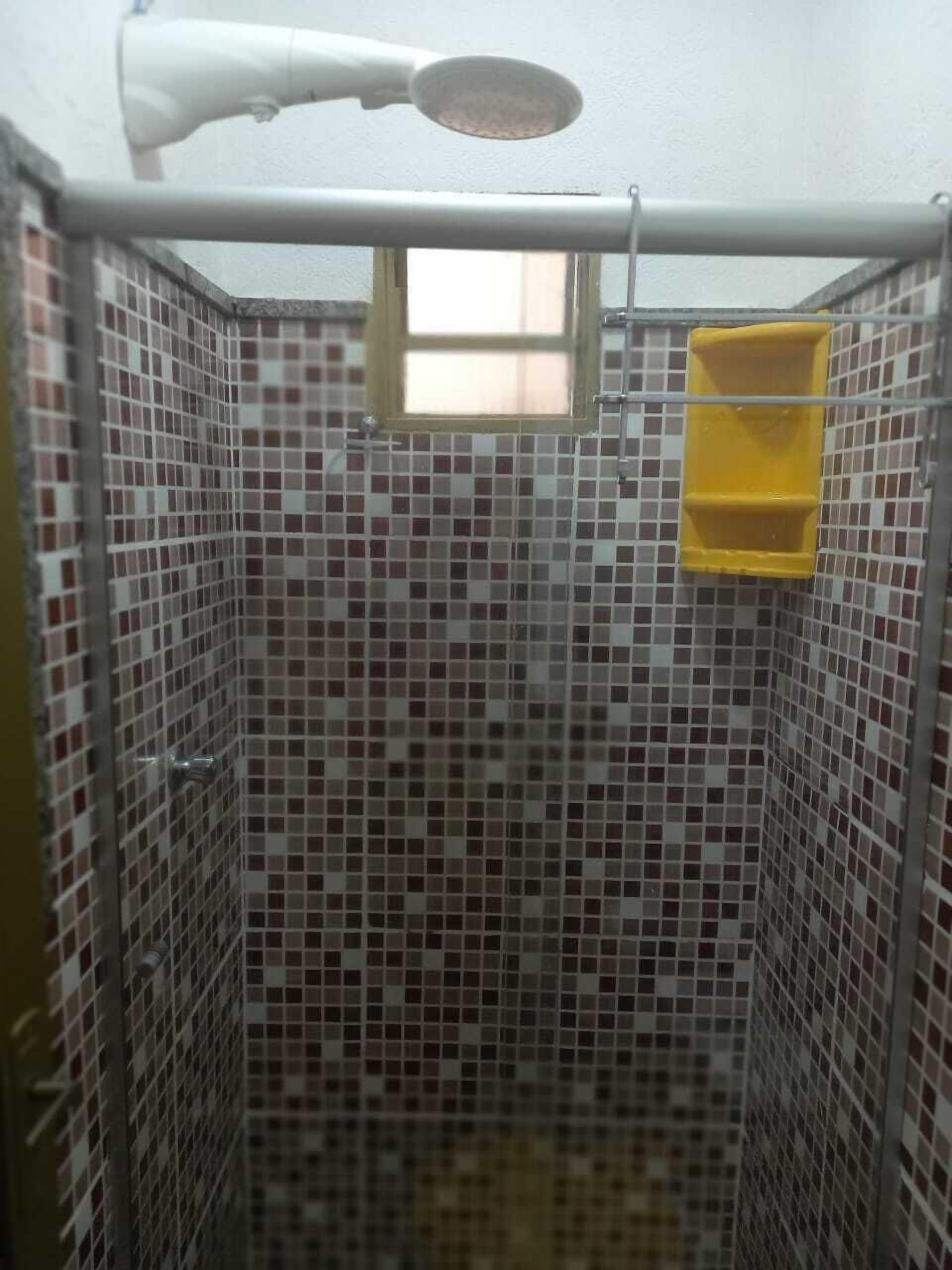 Una cabina de ducha con un cabezal de ducha manual blanco, una ventana pequeña y un jabonera amarilla.