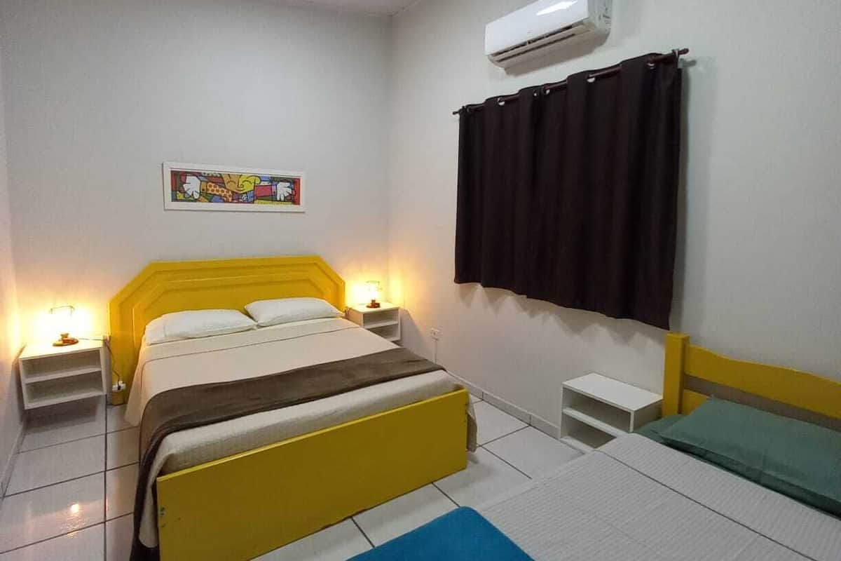 Une chambre d’hôtel avec un lit double, des tables de chevet avec des lampes, un climatiseur fixé au mur et une fenêtre avec des rideaux.