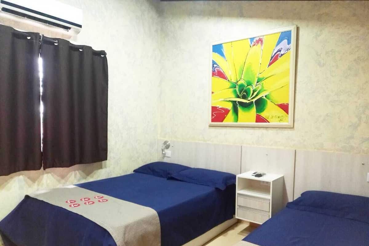 Une chambre d’hôtel avec deux lits, une commode blanche, un tableau au mur et une fenêtre avec des rideaux.