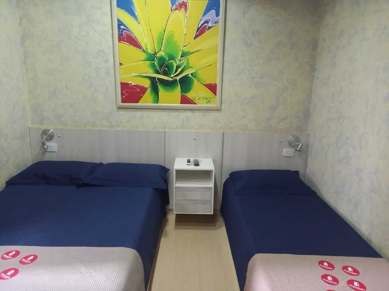Une chambre d’hôtel avec deux lits simples, une petite table de chevet, un tableau accroché au mur et un revêtement de sol de couleur claire.
