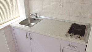 Een keuken met een roestvrijstalen spoelbak, een geïntegreerde kookplaat en lichtgekleurde kastjes.