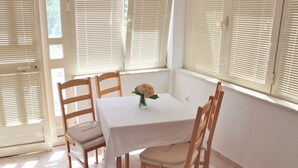 Een eethoek met een tafel gedekt voor vier personen, omringd door houten stoelen en grote ramen met zonwering.