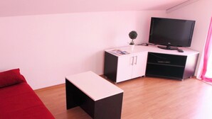 Een kamer met een rode bank, een klein zwart-wit tafeltje, een televisie en een kast met lades.