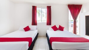 A hotel room with two beds, each with white bedding and red accents, a window with red curtains, and a white tiled floor. - OYO Hotel Cedros (Campeche)