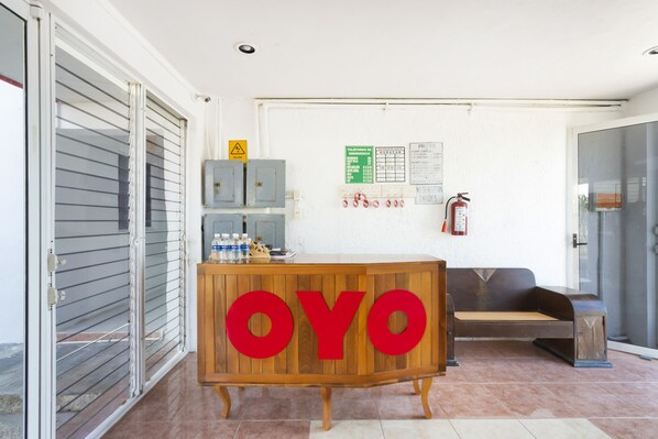 Una recepción con la marca 'OYO', un extintor y datos de contacto de emergencia en la pared.