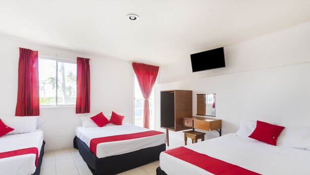 A hotel room with three beds, red curtains, a TV, a desk, and a mirror. - OYO Hotel Cedros (Campeche)