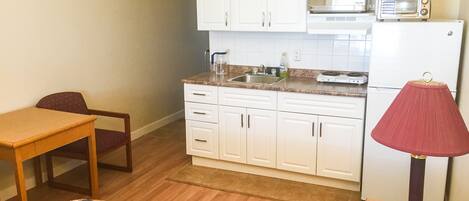 Una cocina compacta con alacenas blancas, un microondas, un tostador y una pequeña mesa.